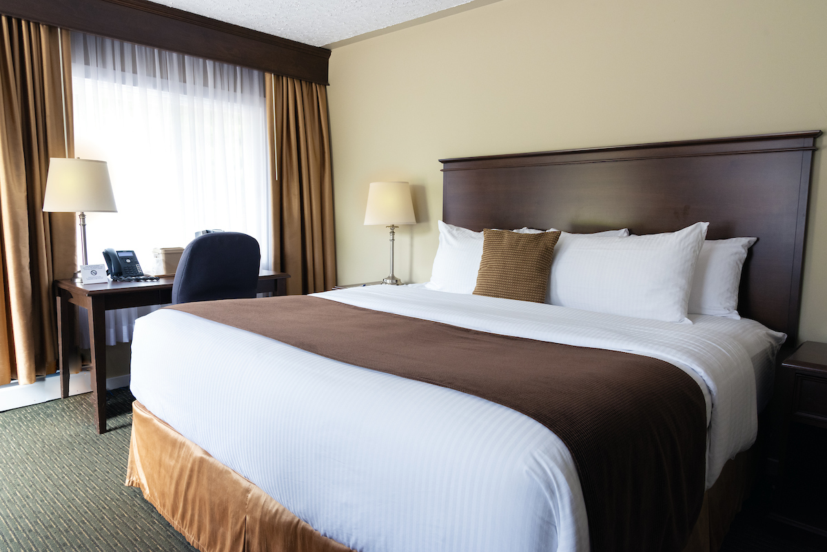 Elegant hotel room at Aurora Inn with a large comfortable bed, crisp white linen, and a work desk, highlighting the inviting accommodations in Annapolis Valley.