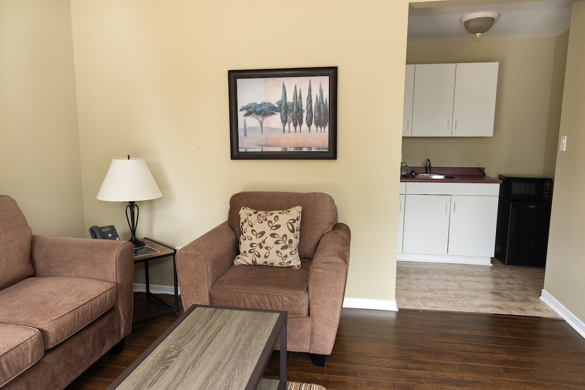 Cozy sitting area with armchair and sofa in an Annapolis Valley Motel room, showcasing a kitchenette in the background.